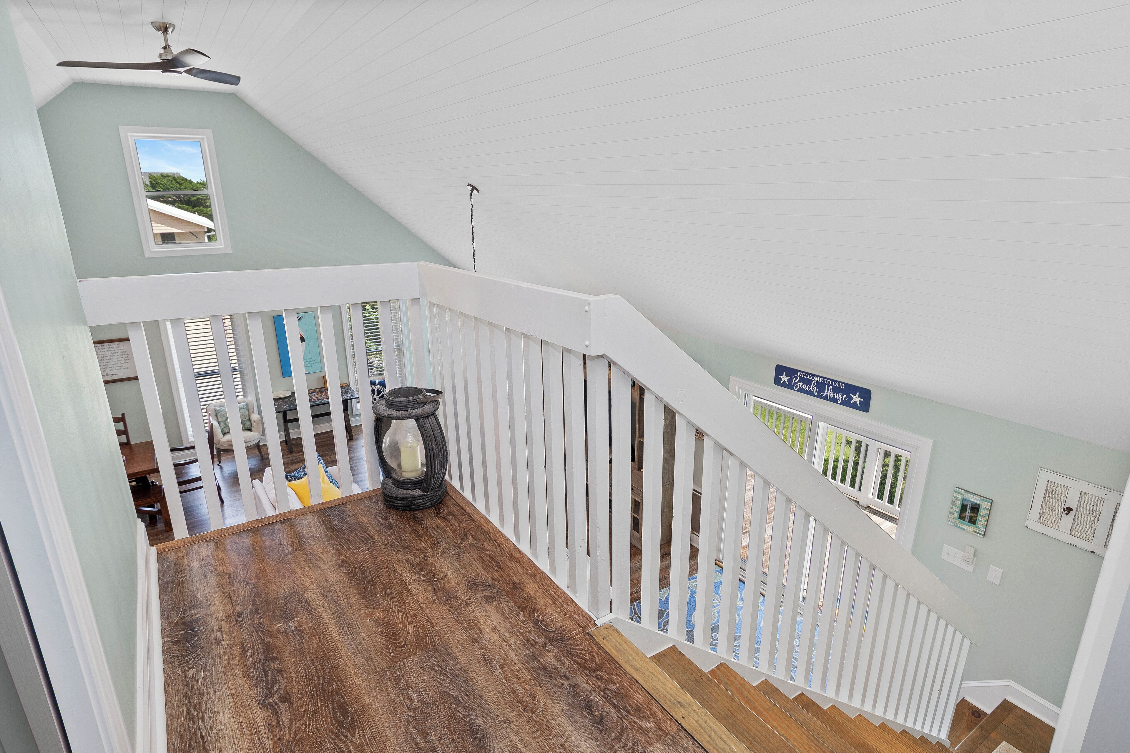 A wooden staircase with white railings, a ceiling fan, and a sign indicating a beach house.