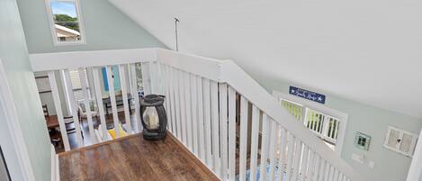 A wooden staircase with white railings, a ceiling fan, and a sign indicating a beach house.