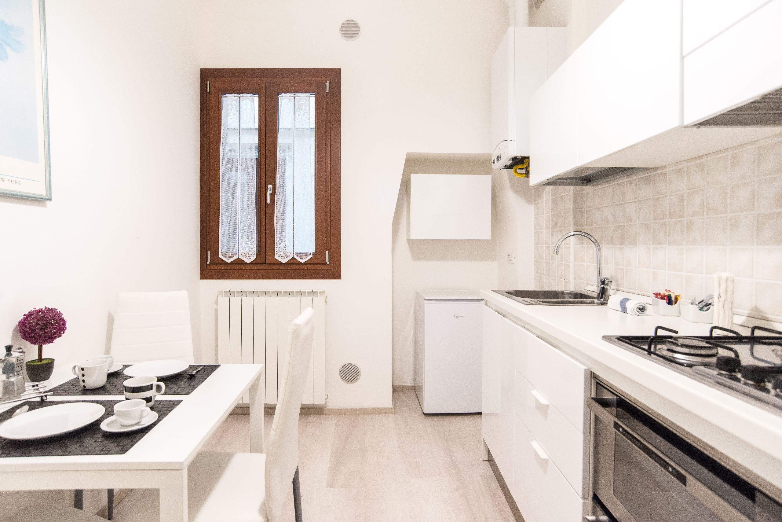 Een kleine keuken met witte kastjes, een ingebouwde oven en een spoelbak.