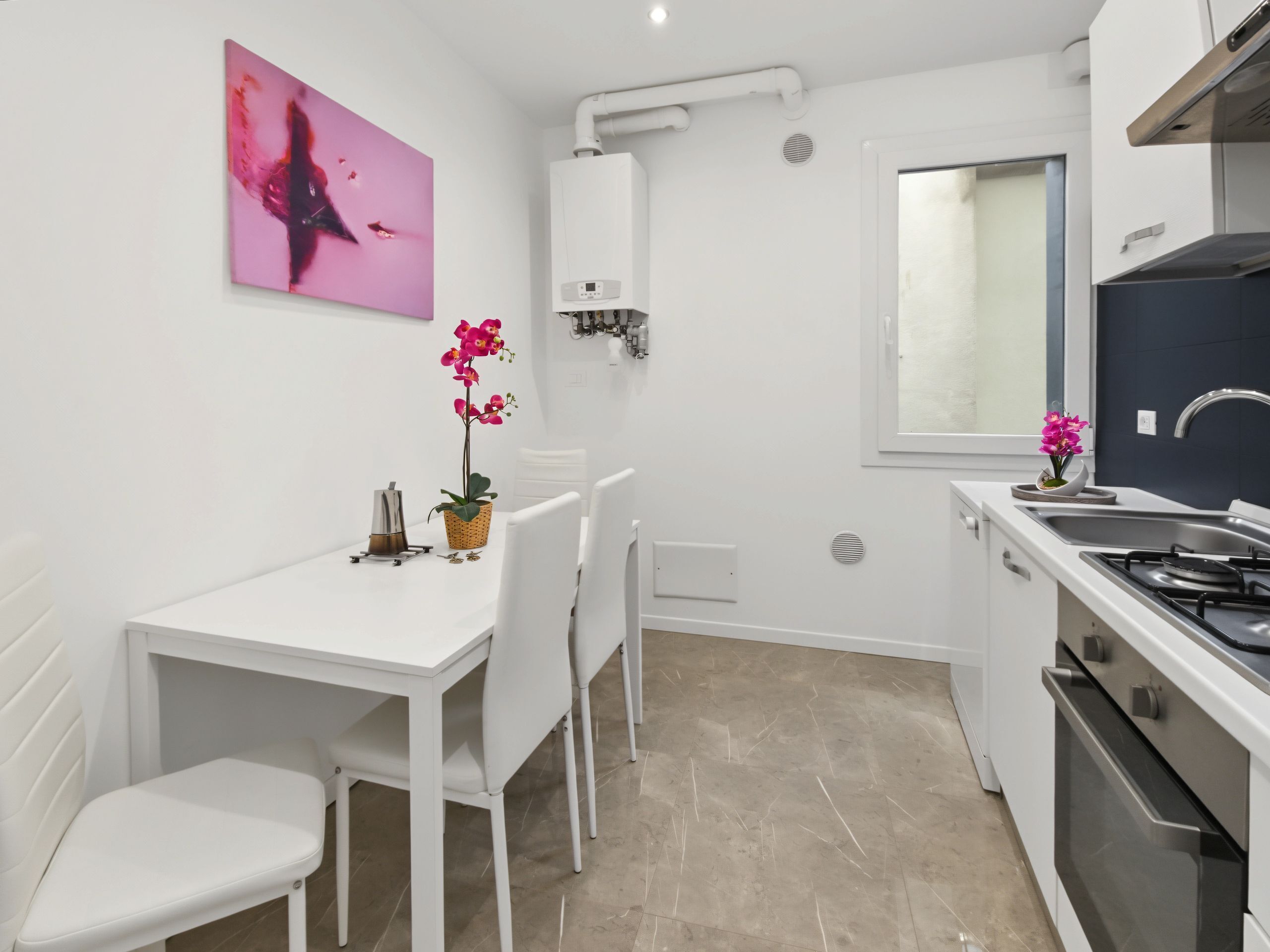 Une cuisine moderne avec des meubles blancs, une cuisinière à gaz, un évier et un coin repas comprenant une table et des chaises blanches.