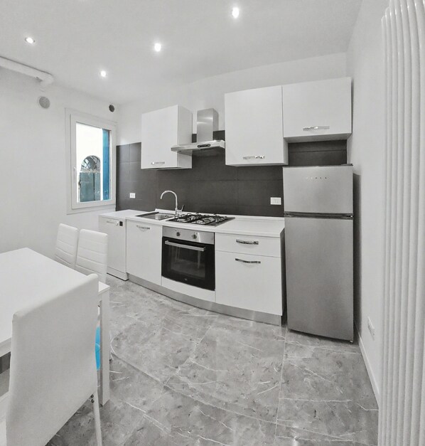 Una cocina moderna con armarios blancos, estufa a gas, horno y refrigerador.