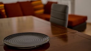 A dining table with a plate in the foreground and a sofa with cushions in the background. - Magic View - WiFi (Venezia)