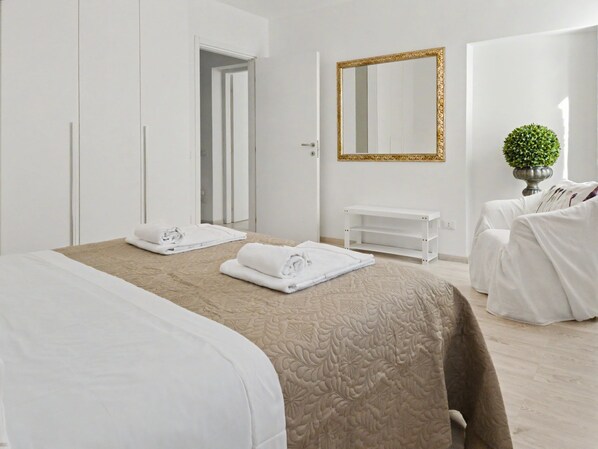 Una habitación de hotel con cama, mesita de noche, espejo, silla y una pequeña planta en maceta.