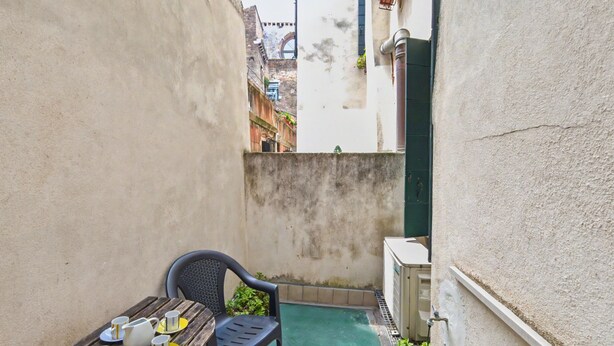 A narrow outdoor space with a wooden table set for two, a plastic chair, and a small pool. - Rialto Dream (Venezia)