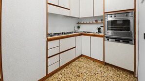 A compact kitchen with white cabinets, a stainless steel oven, and a speckled floor. - Rialto Dream (Venezia)