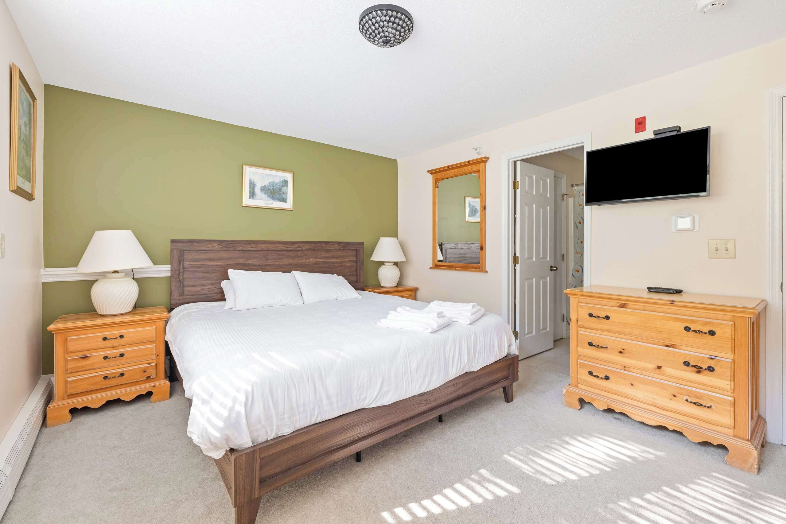 A bedroom with a bed, wooden nightstands, a dresser, a television, and a door.