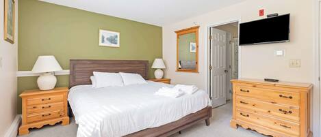 A bedroom with a bed, wooden nightstands, a dresser, a television, and a door.