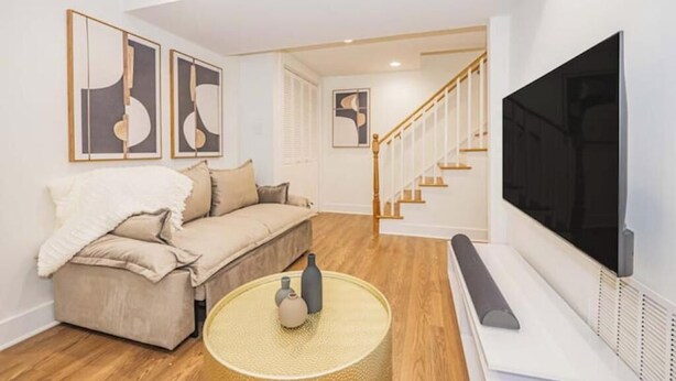 Ein modernes Wohnzimmer mit einem beigefarbenen Sofa, einem runden Couchtisch und einem an der Wand montierten Flachbildfernseher.