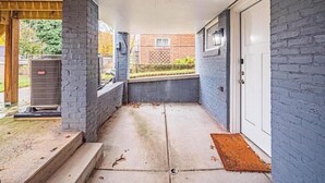 Ein überdachter Außenbereich mit Betonboden, einer Klimaanlage und einer Tür mit Fenster.