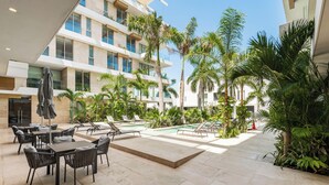 A modern hotel courtyard with outdoor seating, a pool, and palm trees. - Alba Puerto Cancun (Cancun)