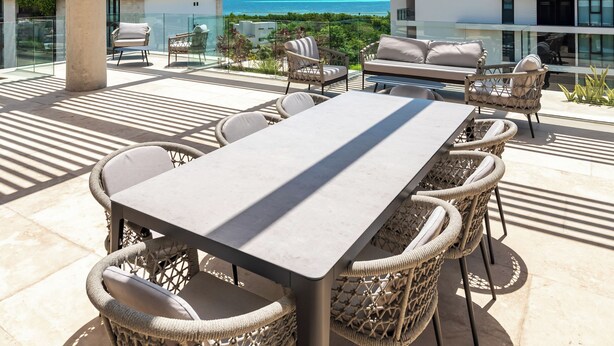 A rooftop terrace with a long table and wicker chairs, overlooking a modern building and the ocean. - Alba Puerto Cancun (Cancun)