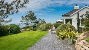 A well-maintained garden with a gravel path leading to a house with a white exterior and a dark roof. - Fron Olau - sleeps 6 guests  in 3 bedrooms (Nefyn)