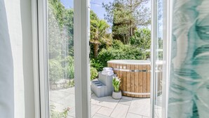 A view through a glass door of a spa area with a wooden hot tub, a small seating area, and a potted plant. - Fron Olau - sleeps 6 guests  in 3 bedrooms (Nefyn)