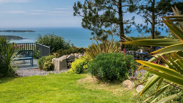 A garden with a bench, a stone wall, and a view of the sea. - Fron Olau - sleeps 6 guests  in 3 bedrooms (Nefyn)