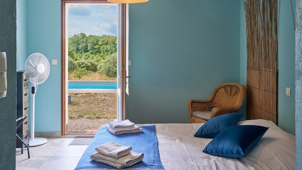 A bedroom with a bed, a chair, a fan, and a view of a natural landscape. - Guest Room 'Bleuet Adapted for PRM' with Private Terrace, Shared Garden and Wi-Fi (Gabillou)