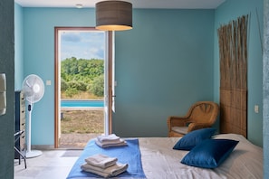 Une chambre à coucher comprenant un lit, une chaise, un ventilateur et donnant sur un paysage naturel.