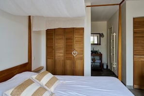 Un dormitorio con un armario de madera, una cama con ropa de cama blanca y un baño visible a través de una puerta abierta.
