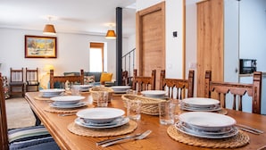 Un comedor con una mesa de madera dispuesta para cuatro personas, rodeada de sillas, con un cuadro en la pared y una escalera al fondo.