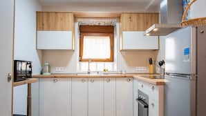 Cocina compacta con ventana, armarios de madera, refrigerador de acero inoxidable y suelo de baldosas.