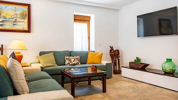 A living room with a green sofa, a coffee table, a TV mounted on the wall, and a painting above the sofa.