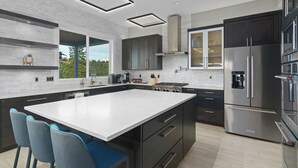 A modern kitchen with a large island, dark cabinetry, stainless steel appliances, and a view of greenery outside. - Spacious 6-bedroom, Views, King Beds, Hot Tub, Game Room near downtown Spokane (Spokane)