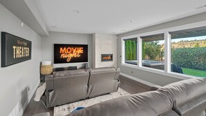 A modern living room with a flat-screen TV, a fireplace, and a large window offering a view of the outdoors. - Spacious 6-bedroom, Views, King Beds, Hot Tub, Game Room near downtown Spokane (Spokane)