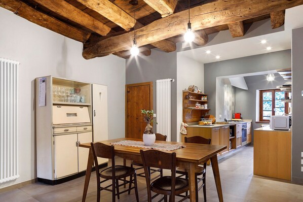 Un comedor con una mesa de madera, sillas, un refrigerador y una cocina al fondo.
