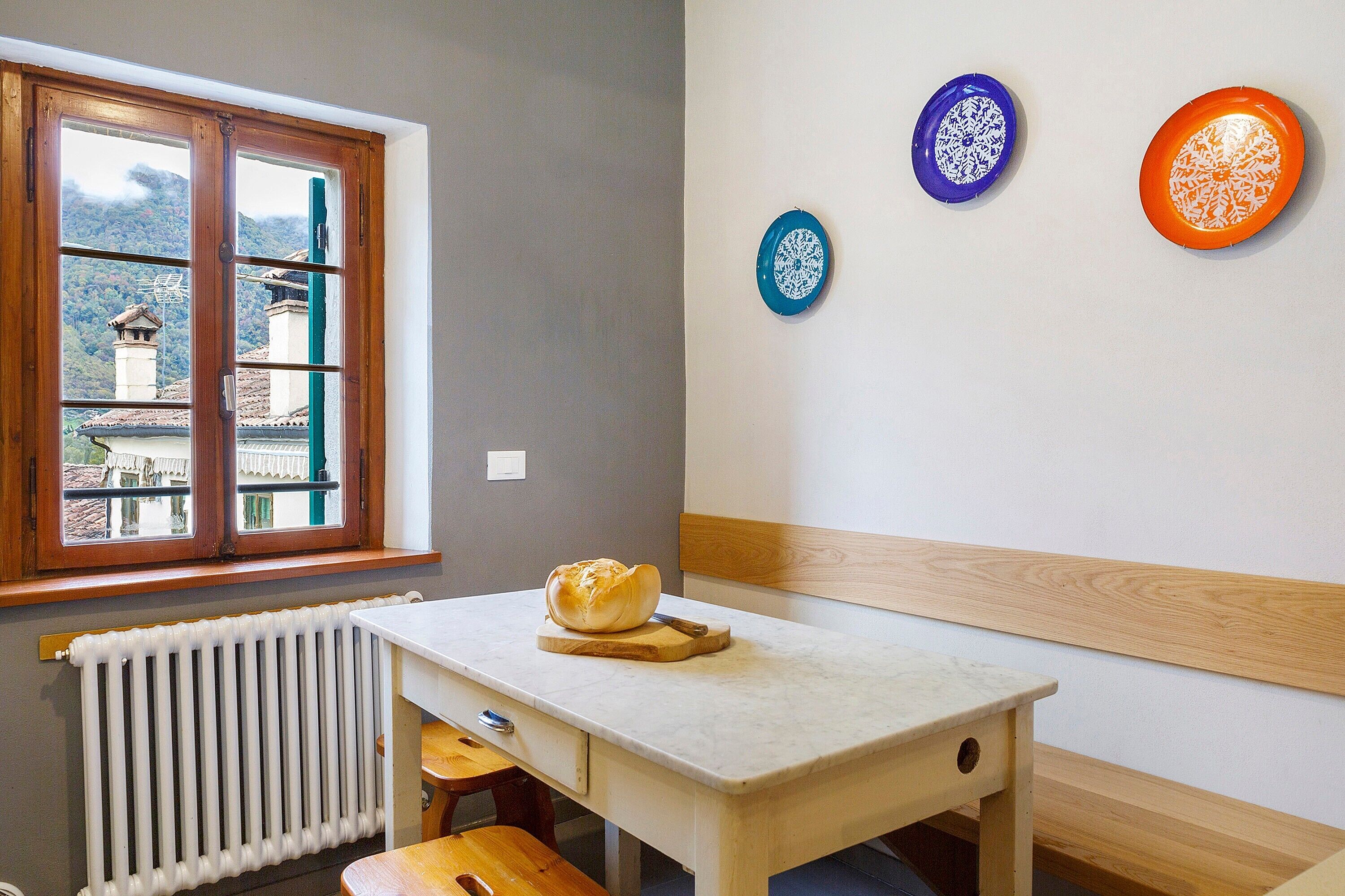 Een keuken met een raam, een tafel met een brood en drie decoratieve borden aan de wand.