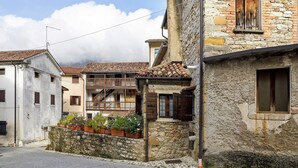 Une rue étroite bordée d’immeubles en pierre, un balcon orné de plantes et un cadre de fenêtre en bois.