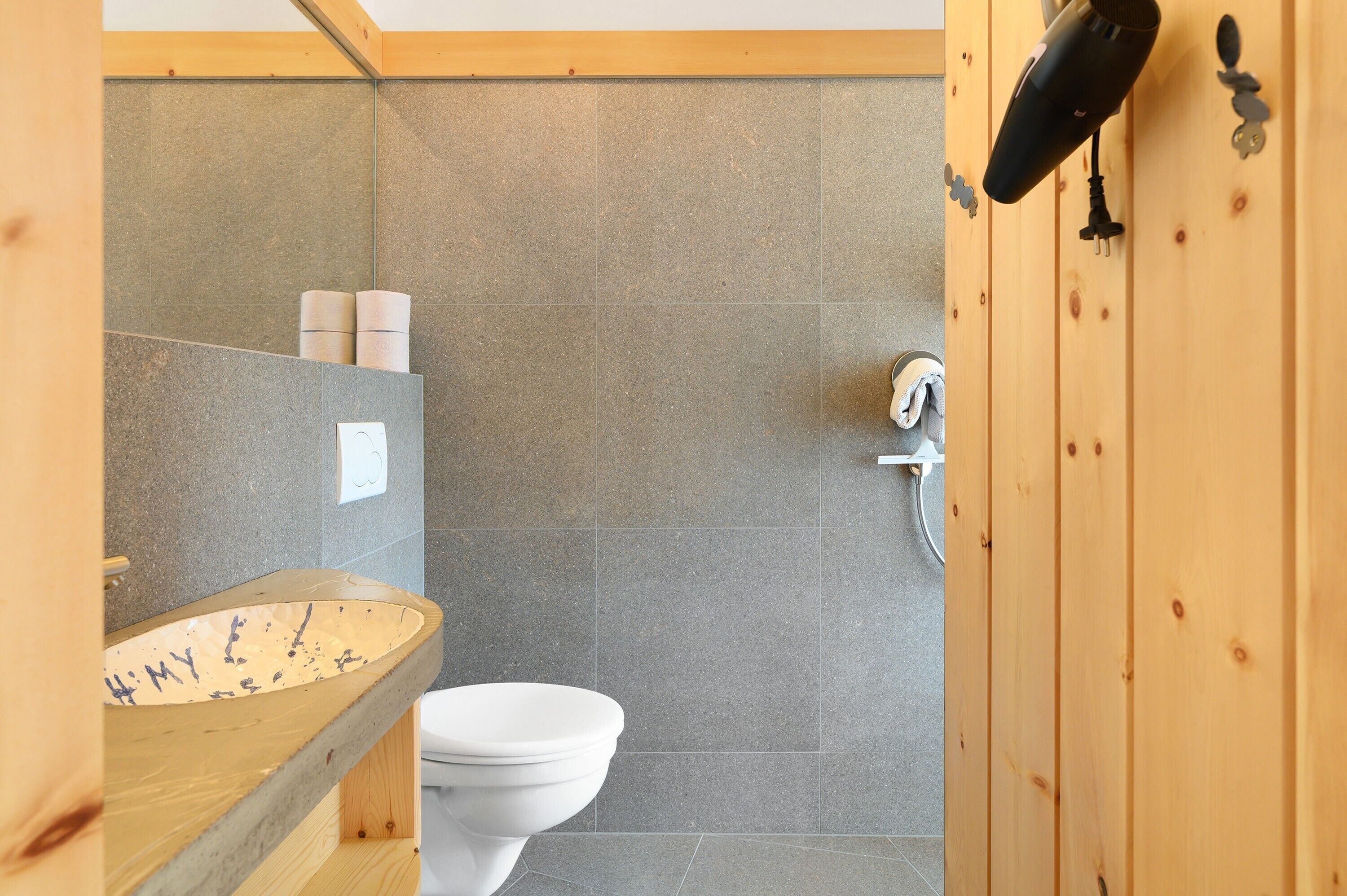 Une salle de bain avec un meuble-lavabo en bois, des toilettes blanches et un espace douche.
