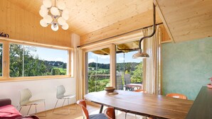 A dining area with a wooden table, chairs, and a view of a green landscape through large windows. - Apartment 'Kesselmoos' with Mountain View, Shared Garden and Wi-Fi (Nova Ponente)