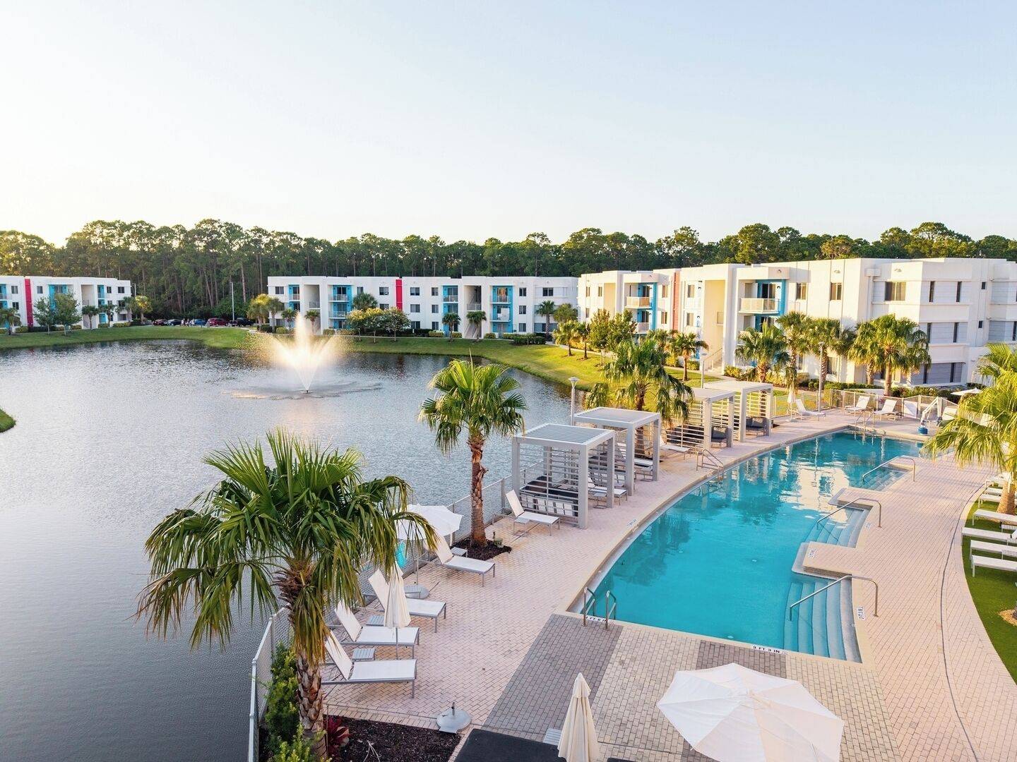 A resort with a swimming pool, lounge chairs, and a fountain.