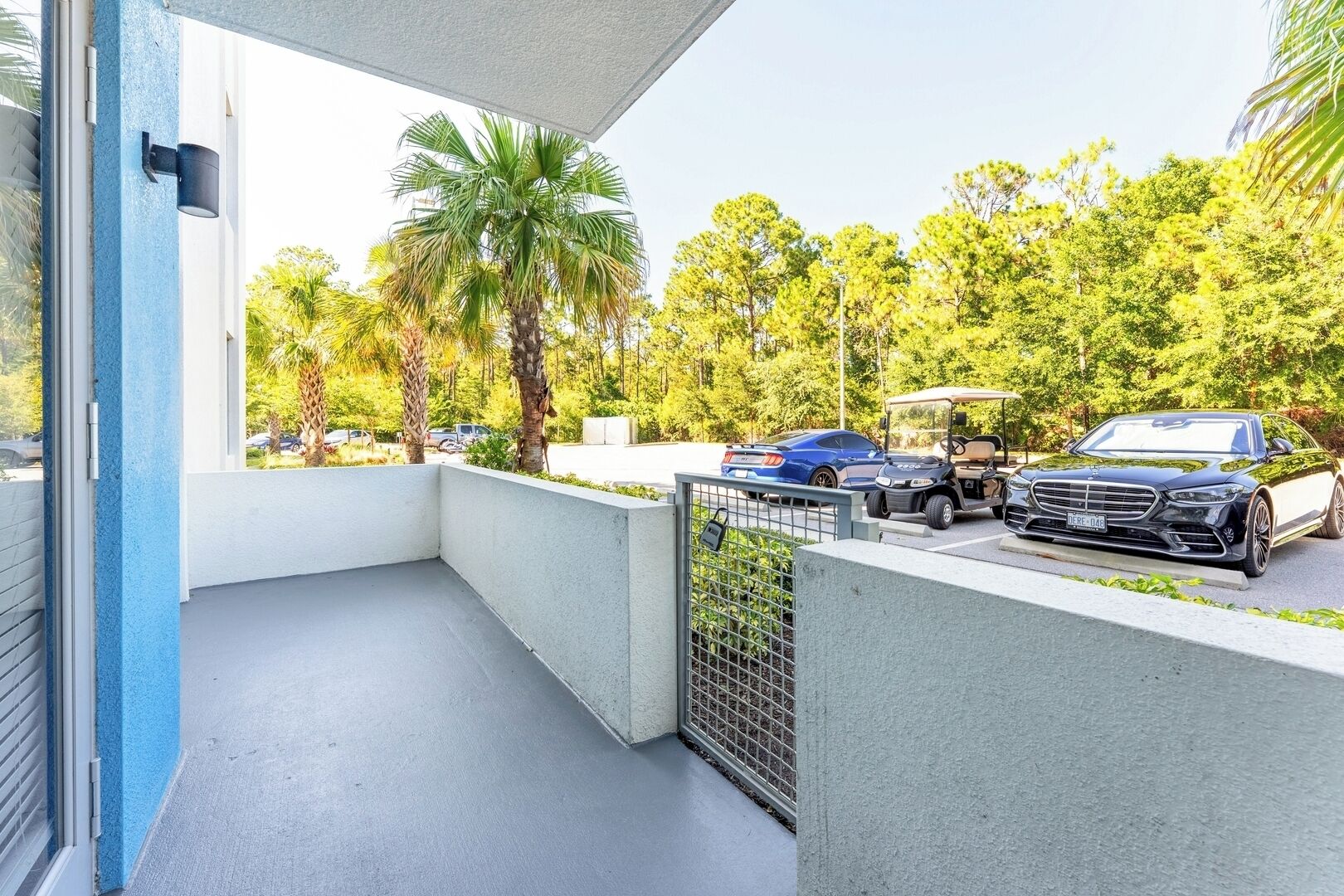 A balcony with a view of a parking area, a golf cart, and a black car.