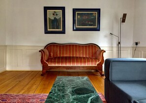 Um quarto com piso de madeira, um sofá de listras vermelhas, uma cadeira azul e duas obras de arte emolduradas na parede.
