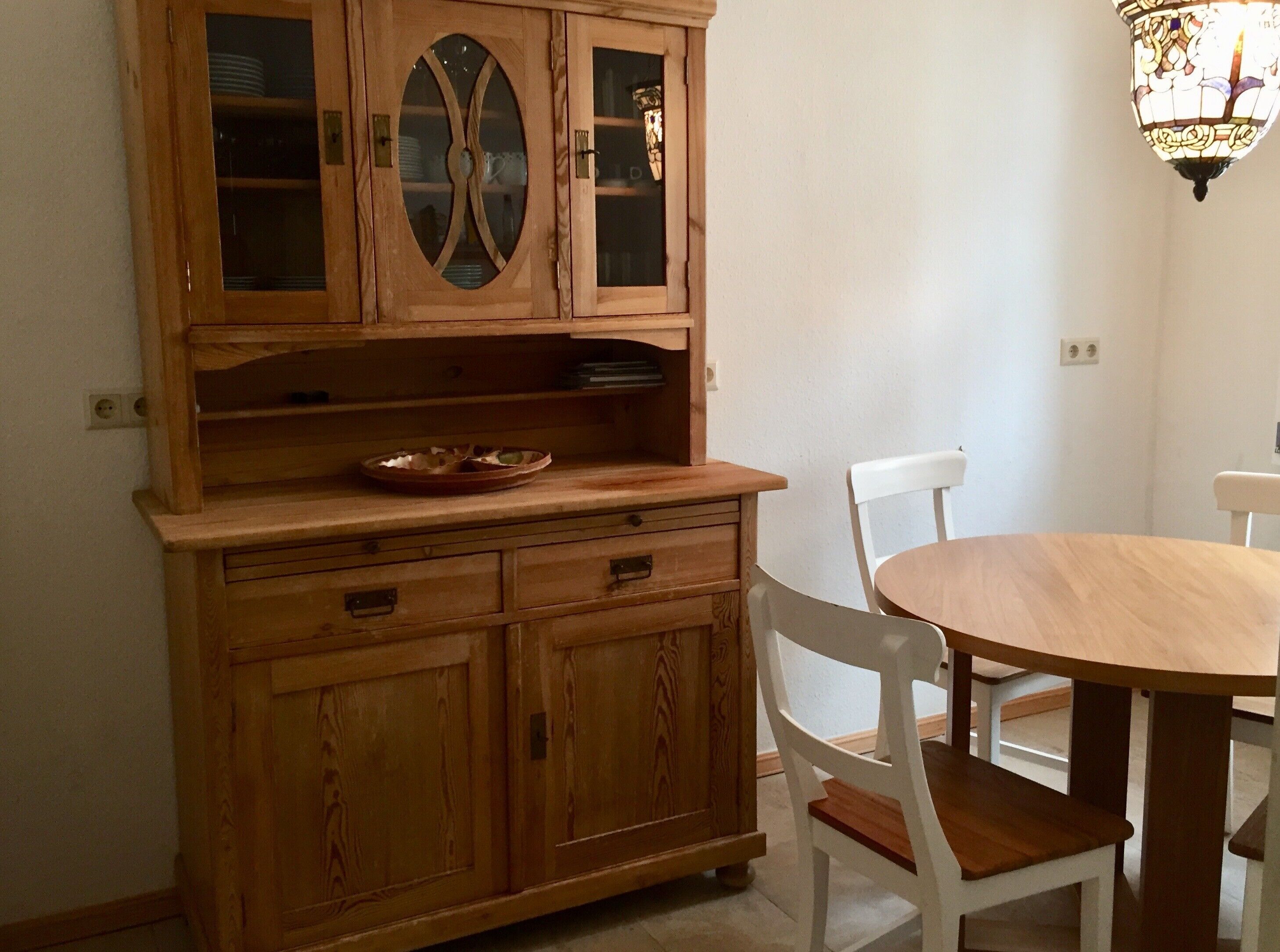 A wooden dining table with chairs, a cabinet with glass doors, and a hanging light fixture.