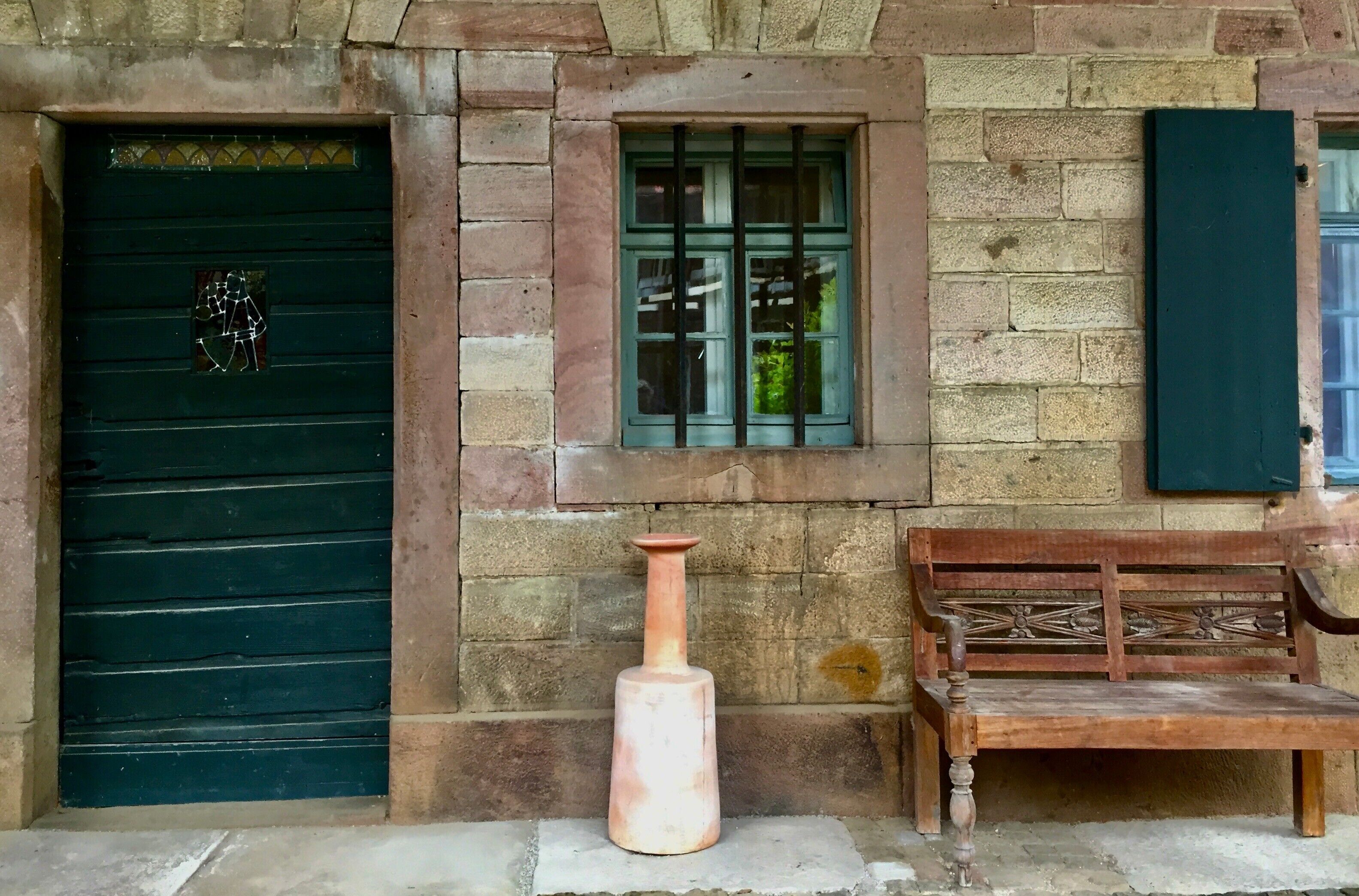 A stone building with a green door, a window with green shutters, and a wooden bench.