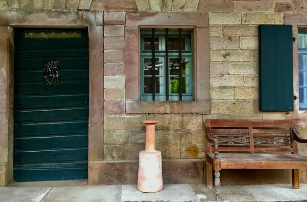 Un bâtiment en pierre avec une porte verte, une fenêtre avec des volets verts et un banc en bois.