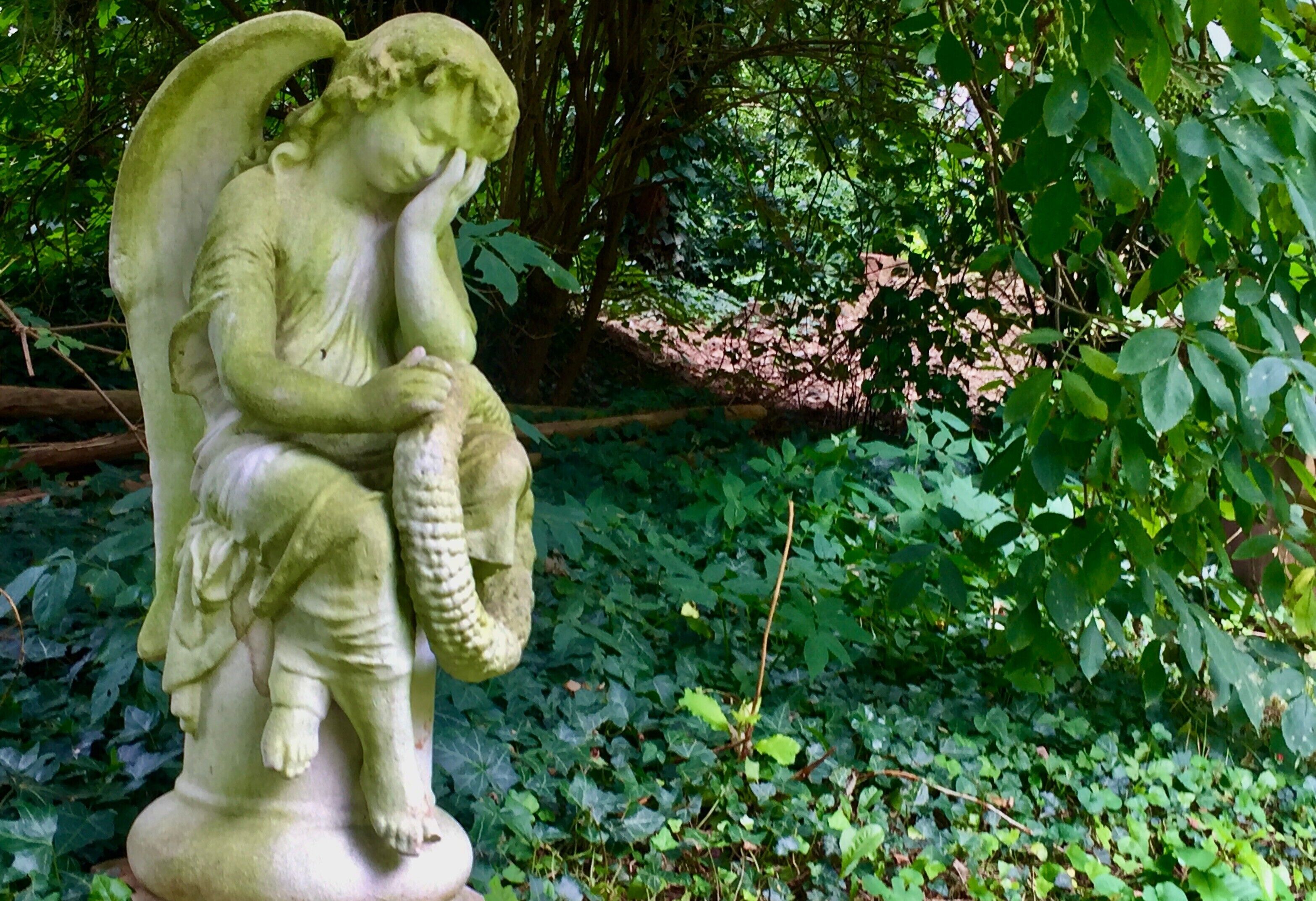 A statue of an angel holding a basket in a garden setting.