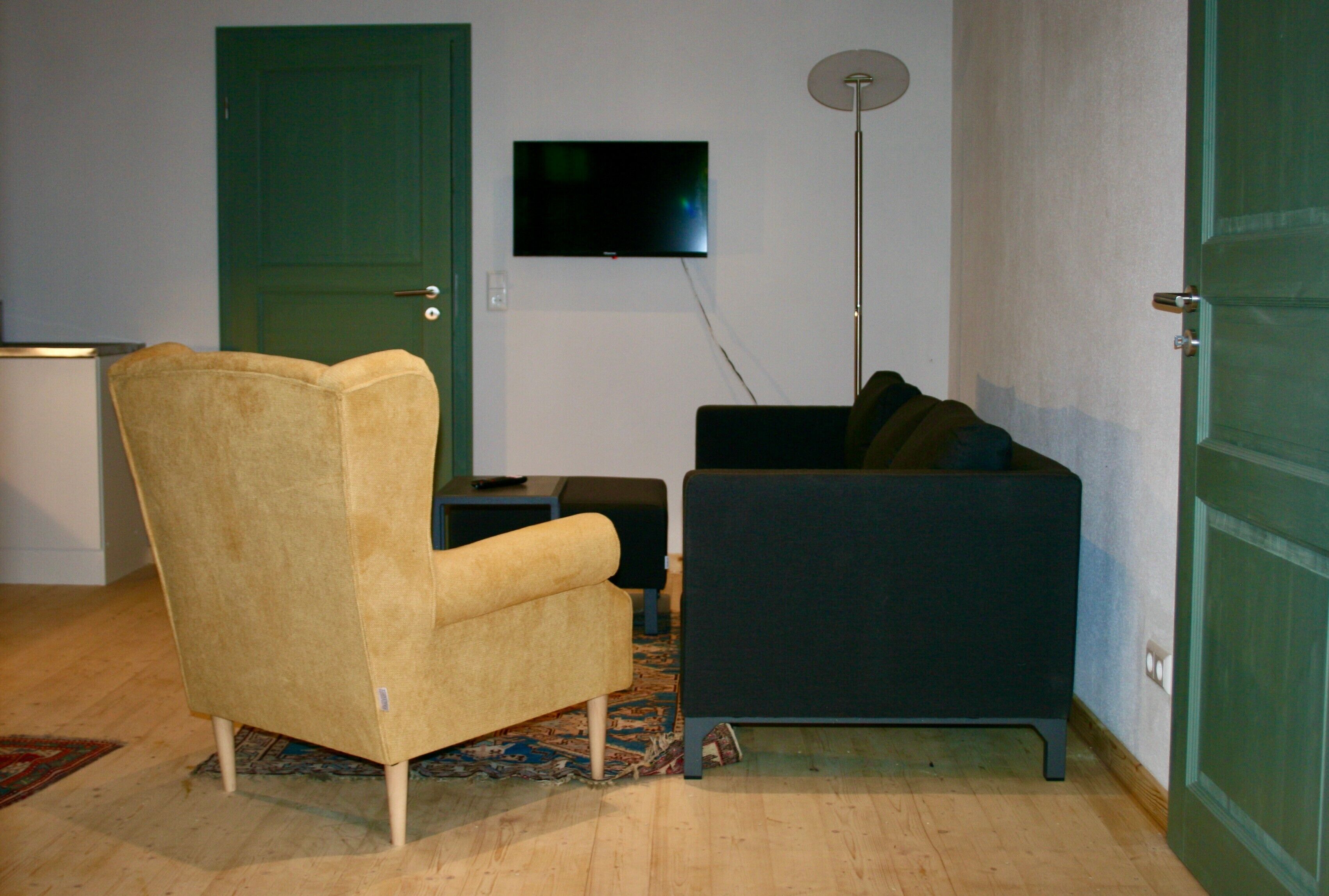 Quarto com poltrona amarela, sofá escuro, TV de tela plana na parede e abajur.