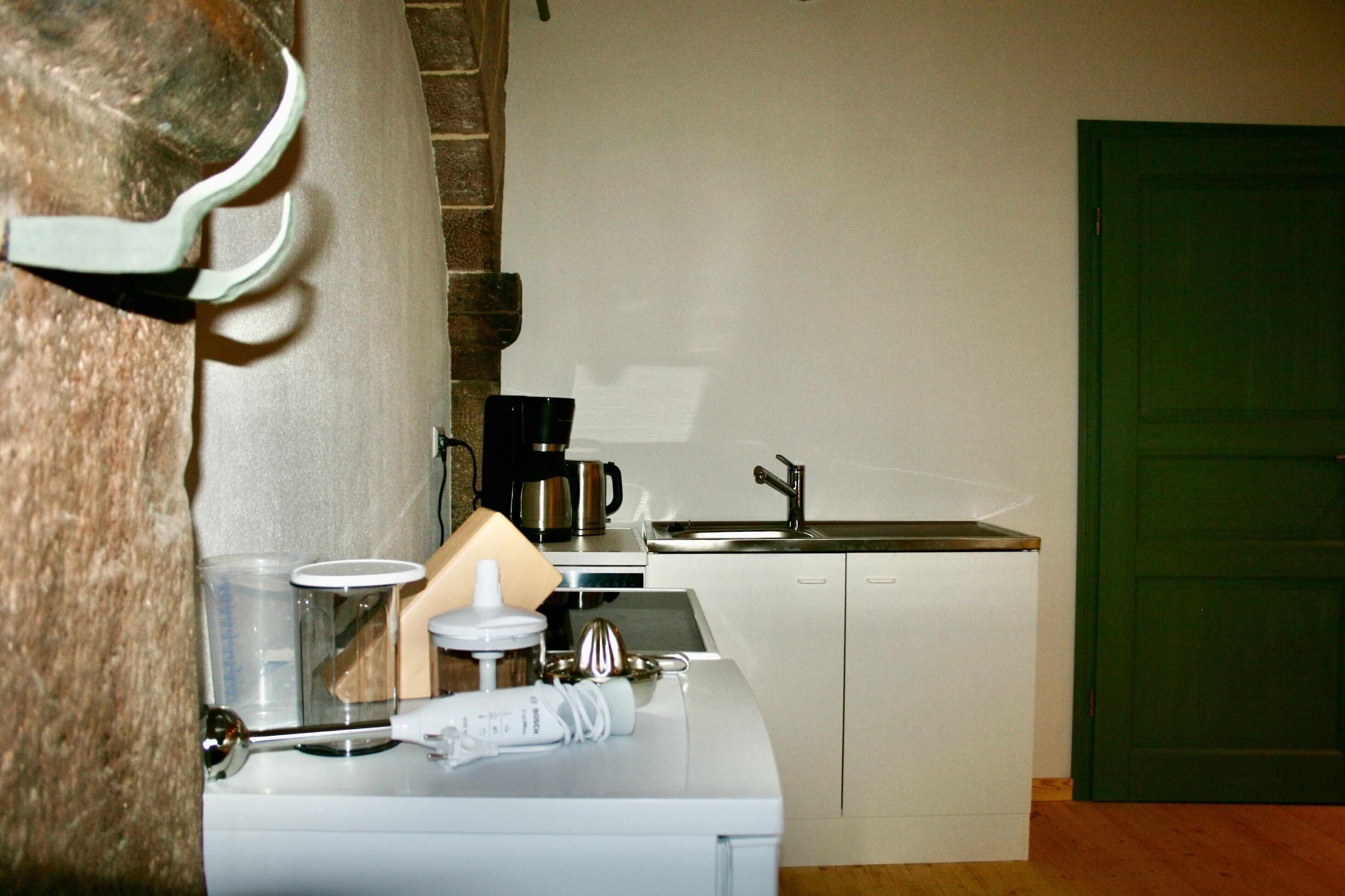 A kitchen with a coffee maker, a sink, and a green door.