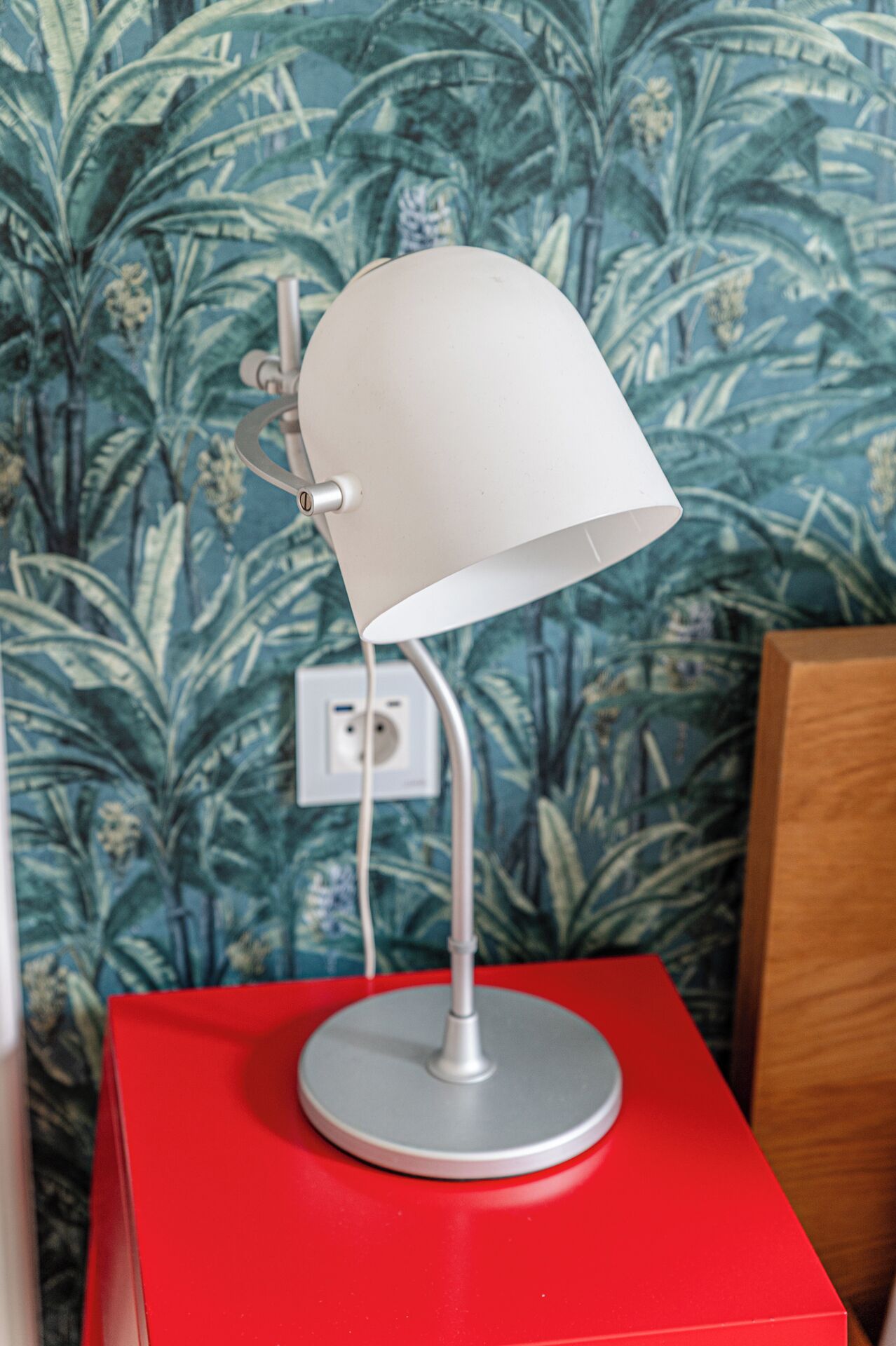 Een bureaulamp met een witte kap op een rode tafel, voor een behangtafel.