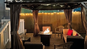 Un patio al aire libre con una mesa de fuego, asientos e iluminación colgante.