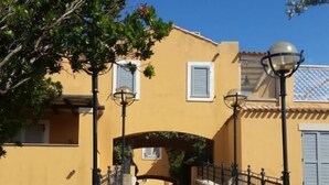 A yellow building with a stone pathway leading to an archway. - Valesmeralda Boutique Rooms  (Arzachena)