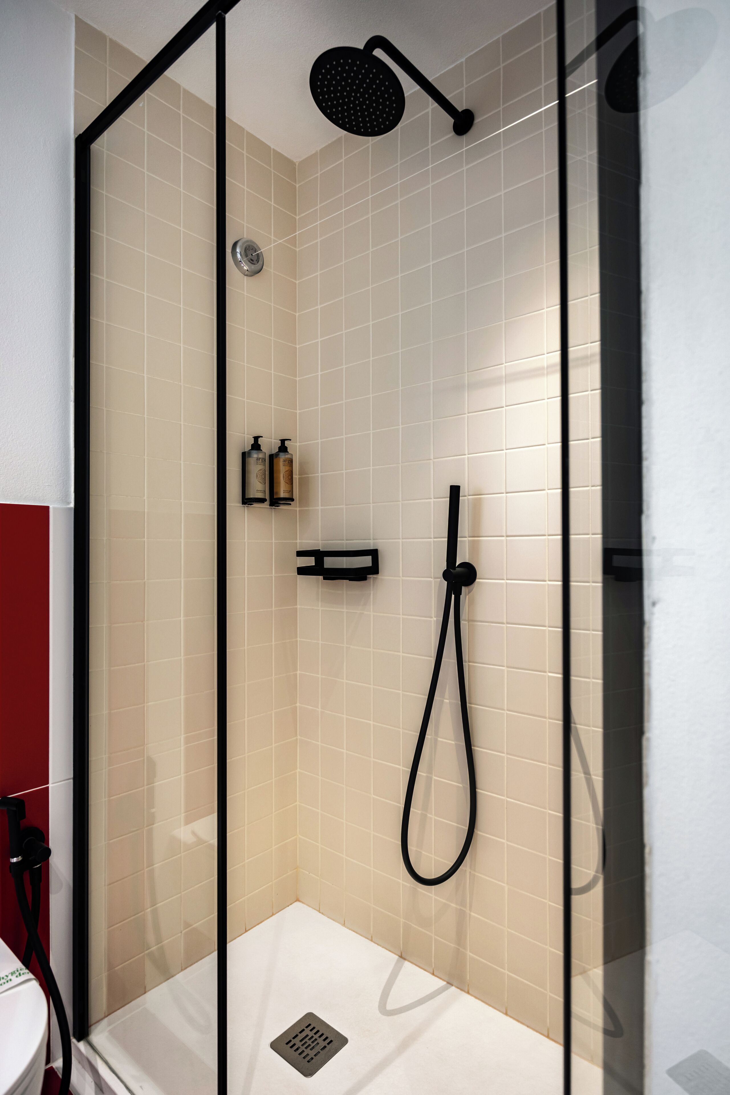 A glass-enclosed shower with a handheld showerhead and a wall-mounted faucet.