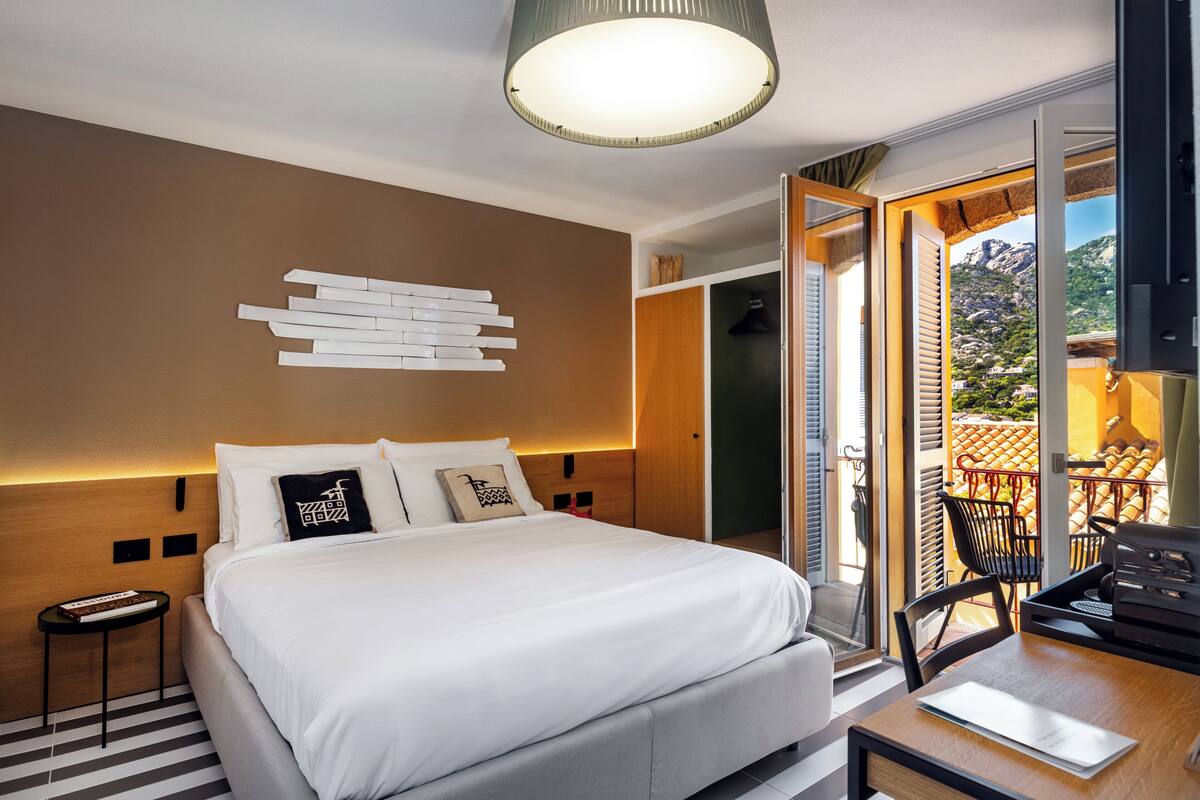 Habitación de hotel moderna con una cama grande, un escritorio con una computadora portátil, vistas al exterior y una obra de arte original en la pared.