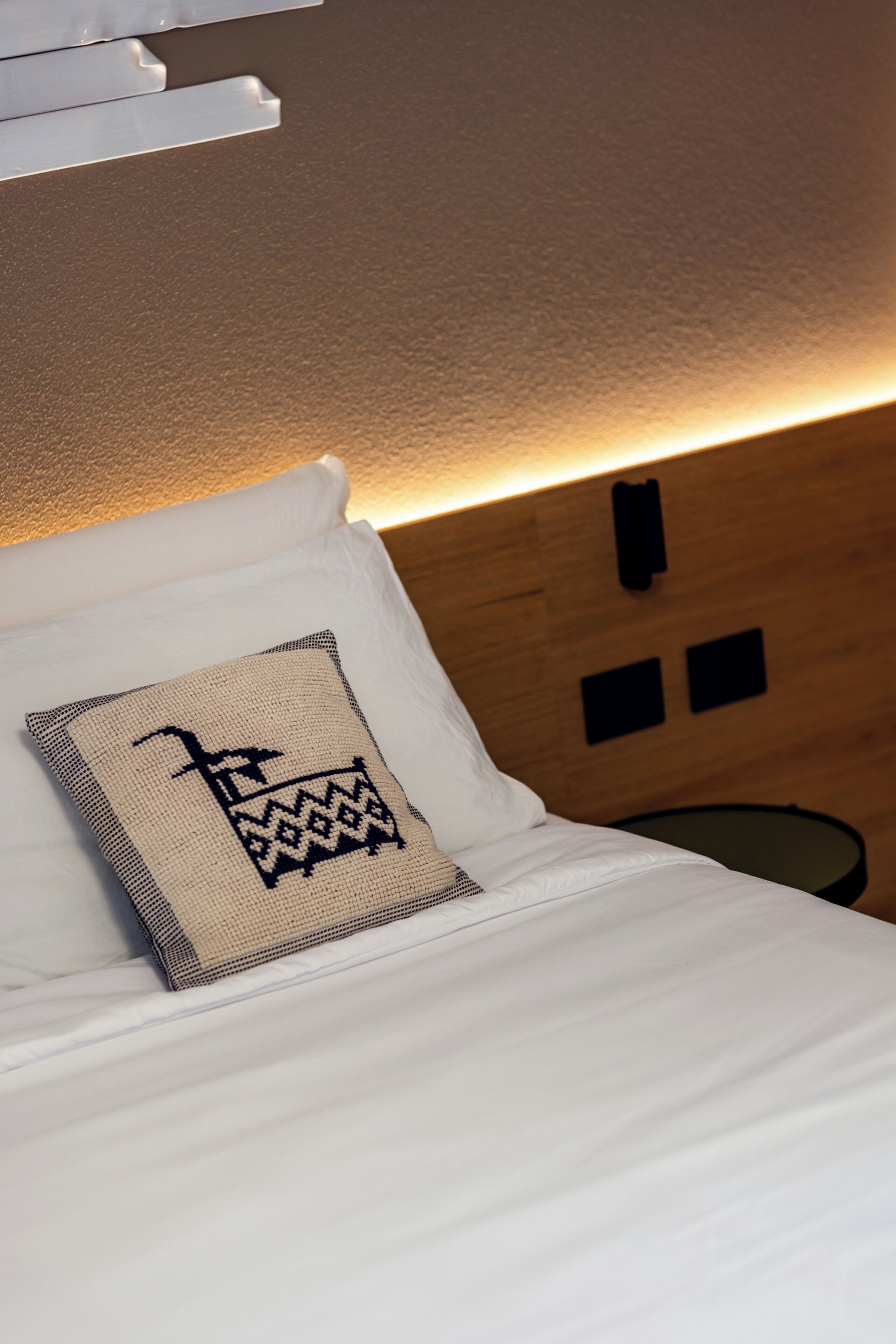 A neatly made bed with a patterned pillow, a wooden headboard, and a wall-mounted phone.