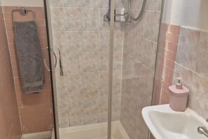 Douche met glazen deur, een handdoekrek met handdoek en een wasbak met zeepdispenser.