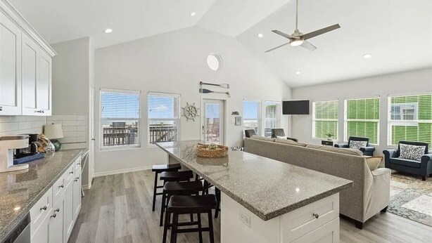 A modern kitchen with a central island, bar stools, and a ceiling fan.