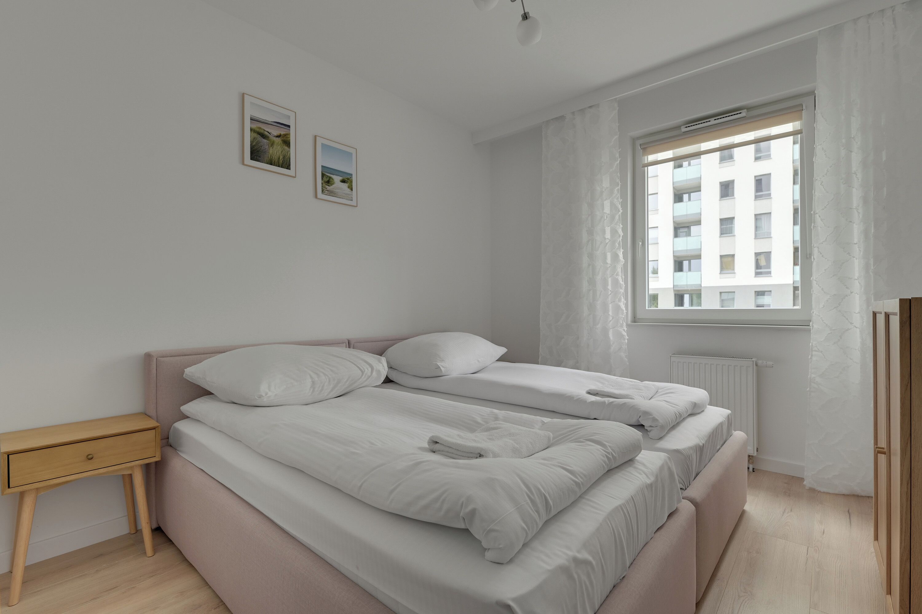 Un dormitorio con dos camas, una mesita de noche de madera y una ventana con cortinas.