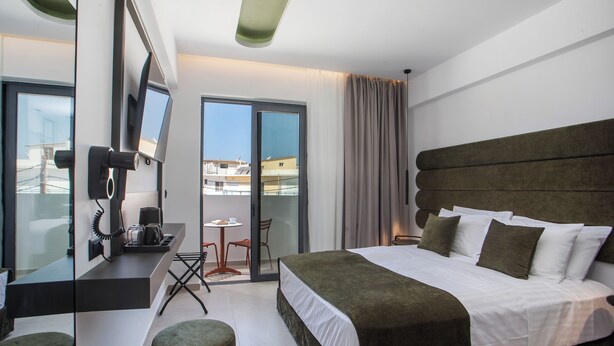 A modern hotel room with a large bed, a desk with a telephone, and a view of the city through the window. - Ermou 44 City Hotel (Faliraki)